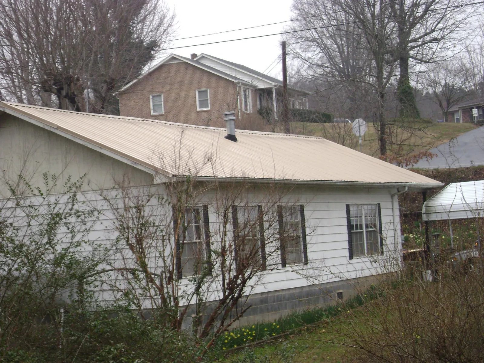 Tan metal roof on a white sided house set into a hillside — Commercial Roofing by Roofing Brothers in San Jose